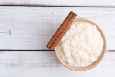 Photo of Tasty rice pudding with cinnamon on white wooden table, top view. Space for text