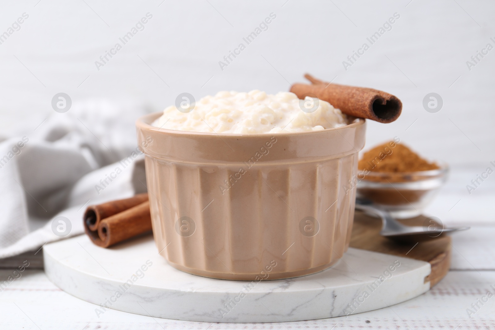 Photo of Tasty rice pudding with cinnamon served on white wooden table, closeup