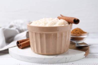 Photo of Tasty rice pudding with cinnamon served on white wooden table, closeup