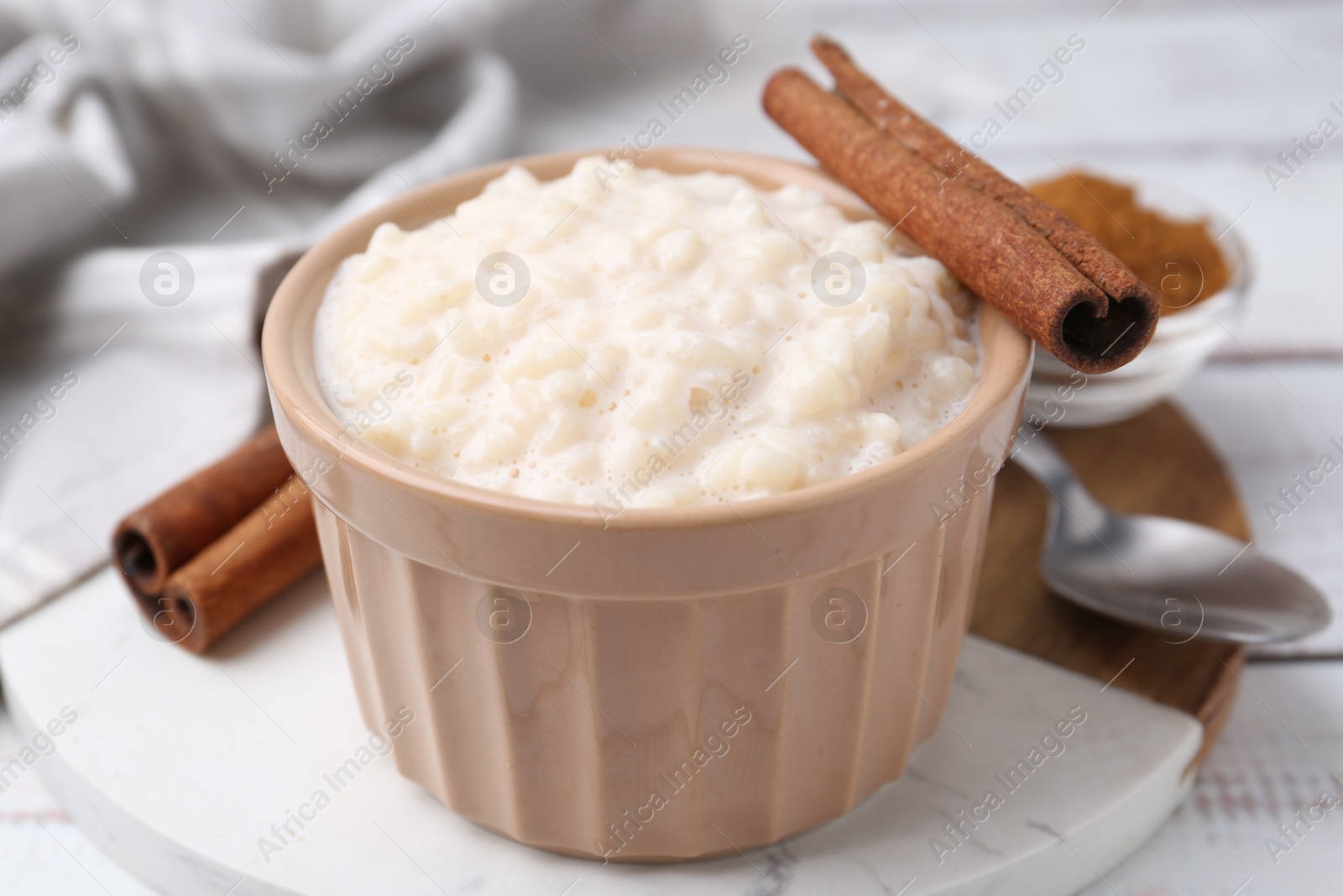 Photo of Tasty rice pudding with cinnamon served on white wooden table, closeup