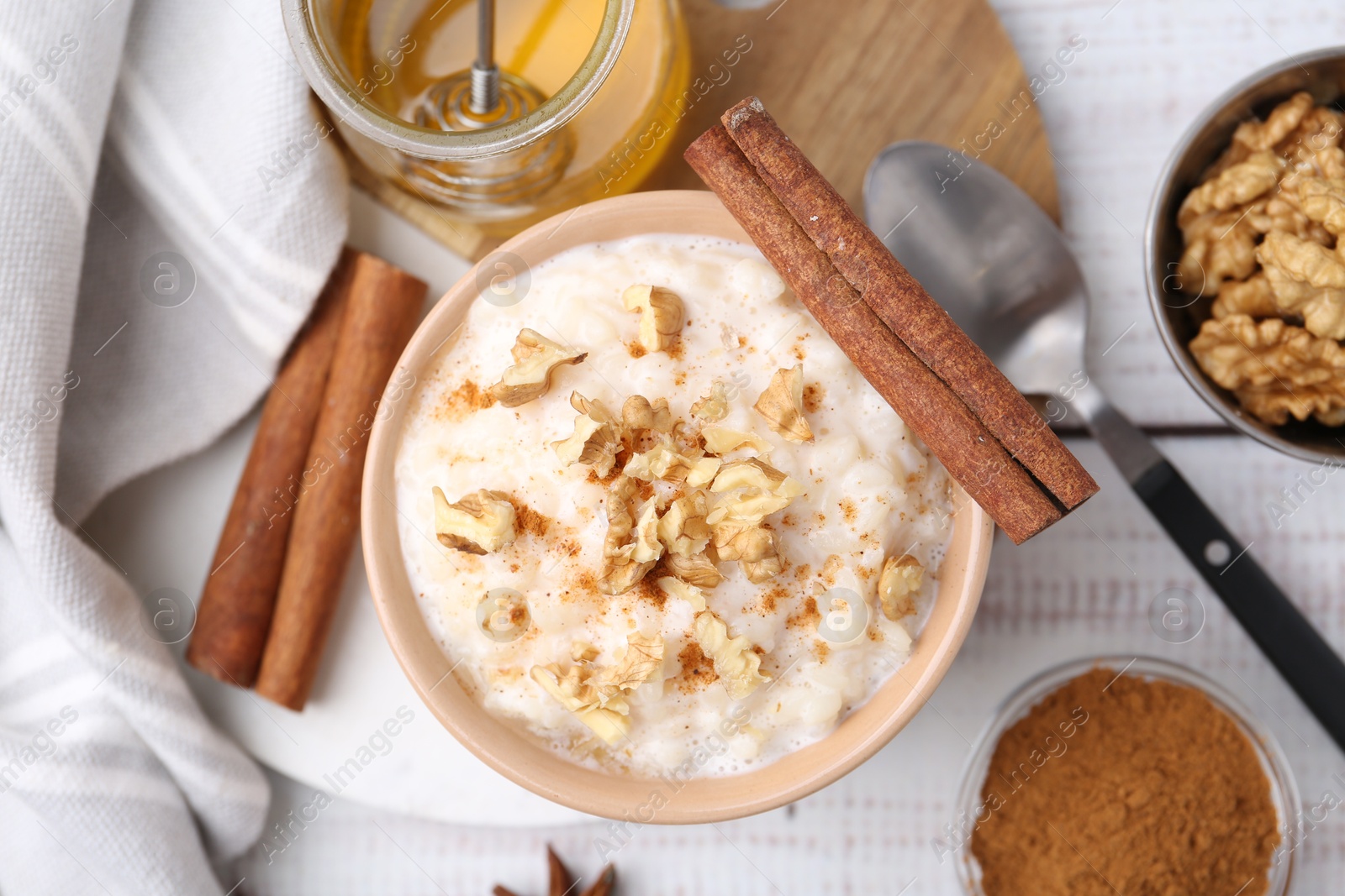 Photo of Tasty rice pudding with cinnamon served on white wooden table, flat lay