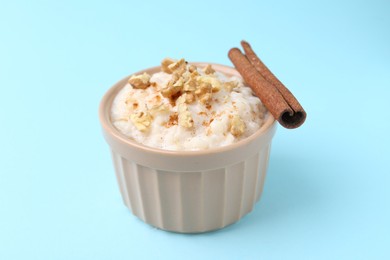 Photo of Tasty rice pudding with walnuts and cinnamon on light blue background, closeup