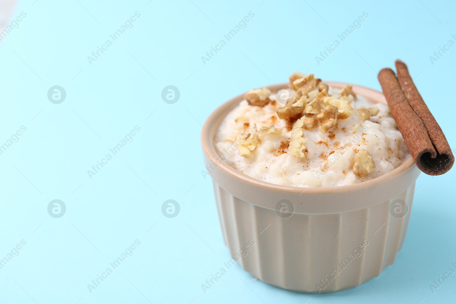 Photo of Tasty rice pudding with walnuts and cinnamon on light blue background, closeup. Space for text