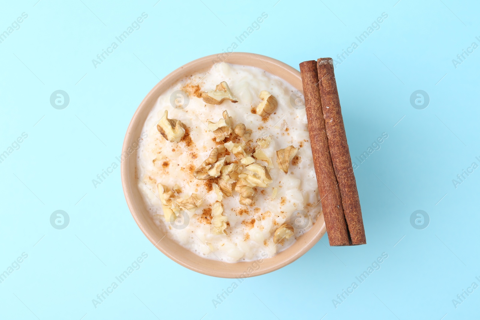 Photo of Tasty rice pudding with walnuts and cinnamon on light blue background, top view