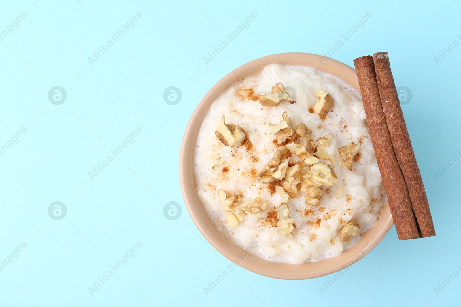 Photo of Tasty rice pudding with walnuts and cinnamon on light blue background, top view. Space for text