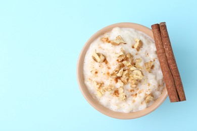 Photo of Tasty rice pudding with walnuts and cinnamon on light blue background, top view. Space for text