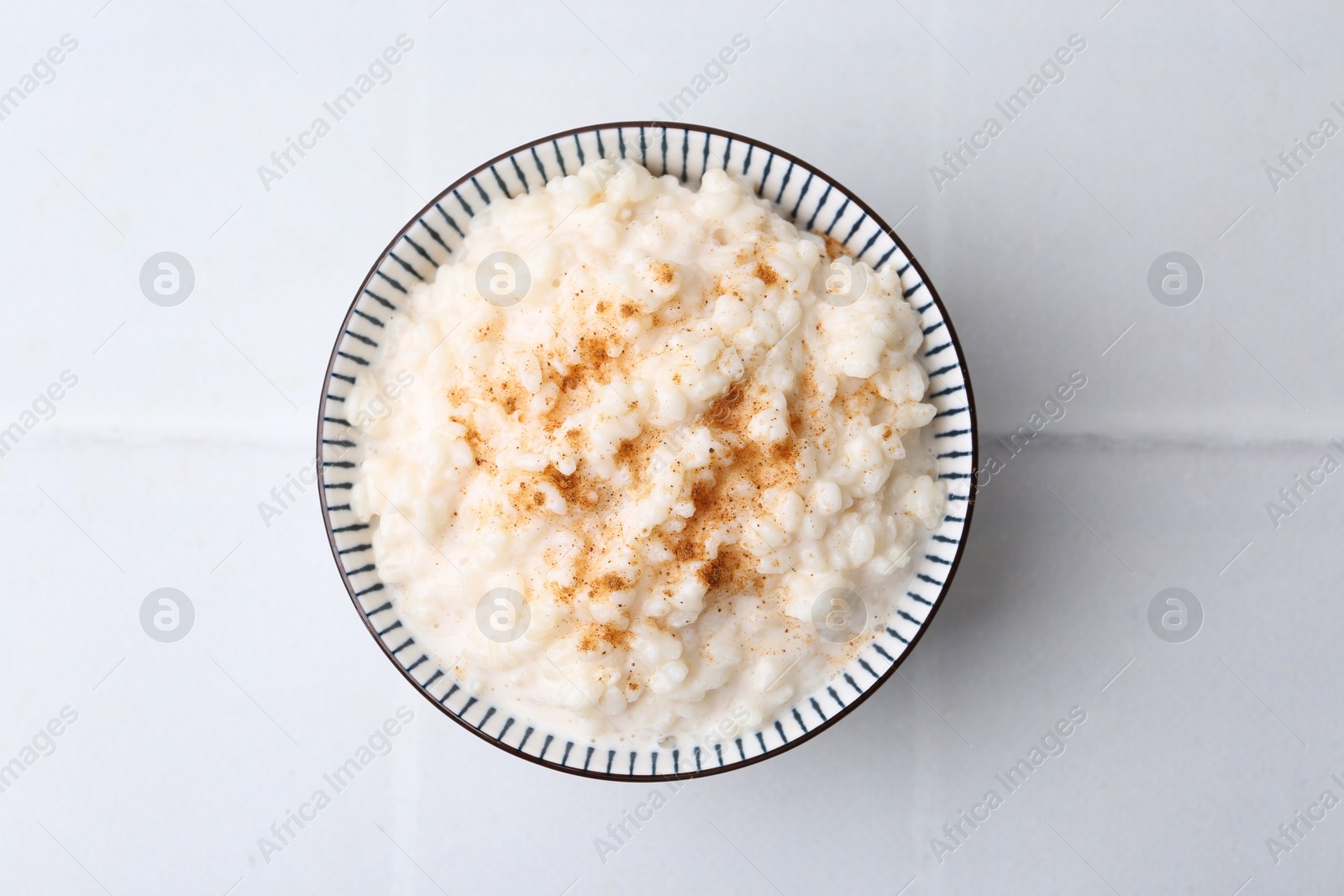 Photo of Tasty rice pudding with cinnamon on white tiled table, top view