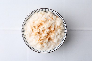 Photo of Tasty rice pudding with cinnamon on white tiled table, top view