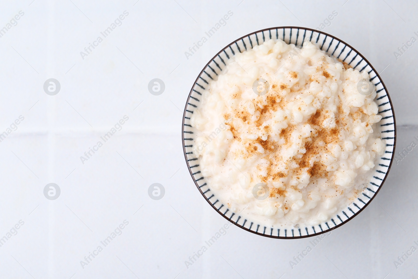 Photo of Tasty rice pudding with cinnamon on white tiled table, top view. Space for text