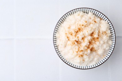 Photo of Tasty rice pudding with cinnamon on white tiled table, top view. Space for text