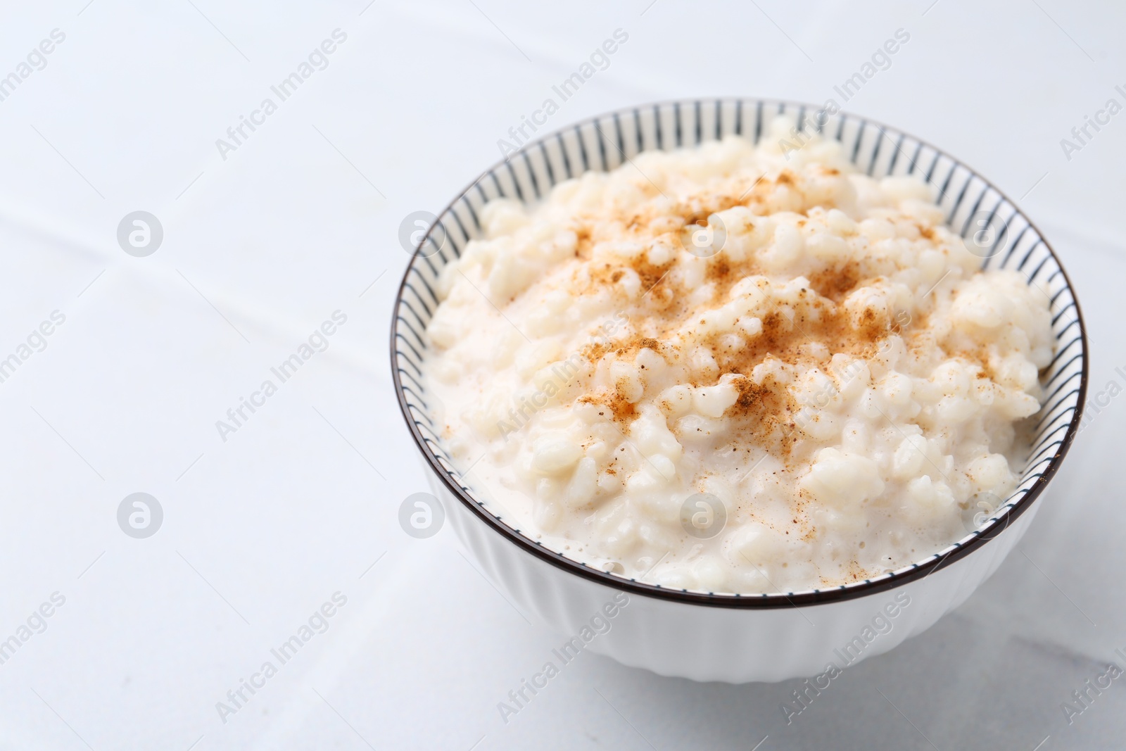 Photo of Tasty rice pudding with cinnamon on white tiled table, closeup