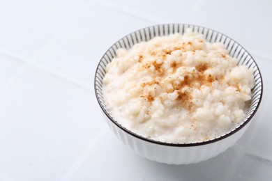 Photo of Tasty rice pudding with cinnamon on white tiled table, closeup