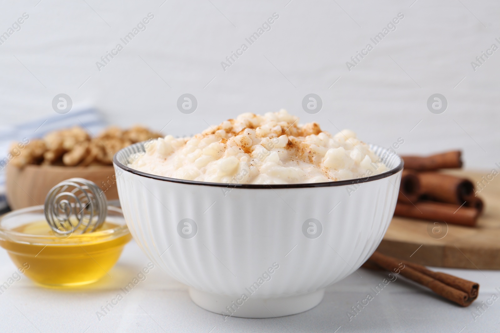 Photo of Tasty rice pudding with cinnamon served on white tiled table, closeup