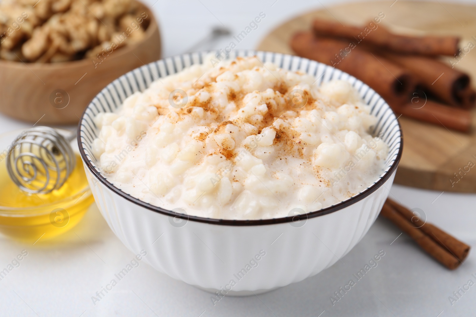 Photo of Tasty rice pudding with cinnamon served on white tiled table, closeup