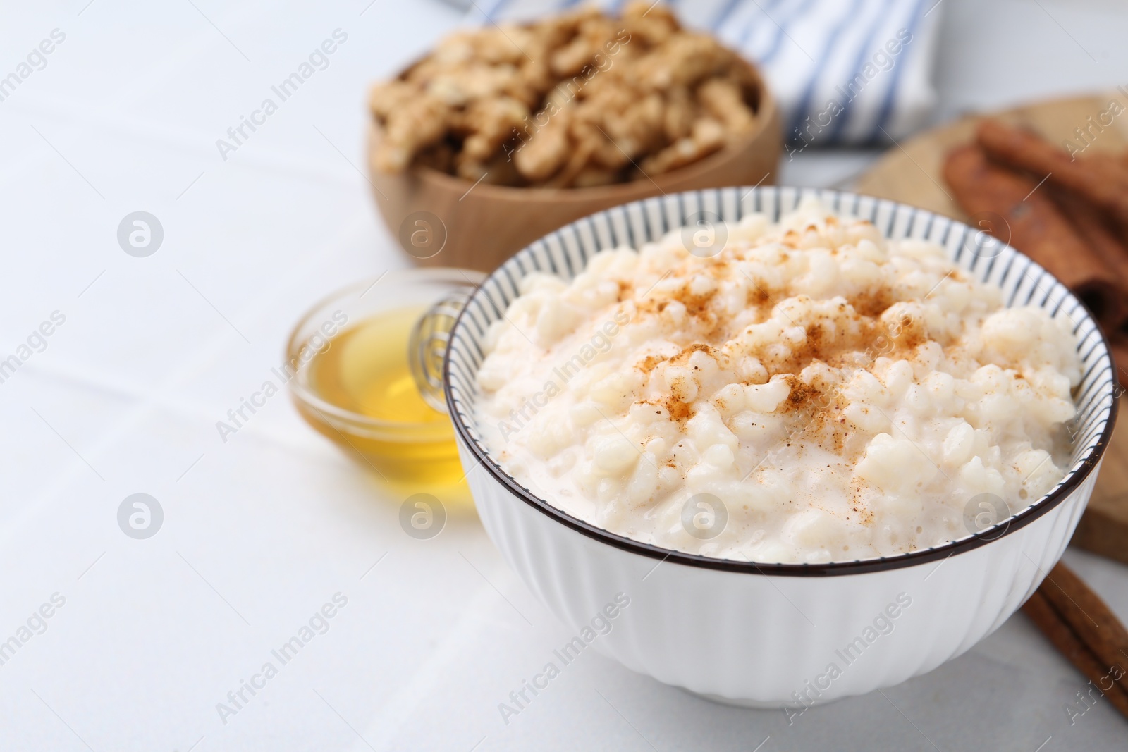 Photo of Tasty rice pudding with cinnamon served on white tiled table, closeup