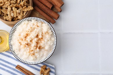 Photo of Tasty rice pudding with cinnamon served on white tiled table, flat lay. Space for text