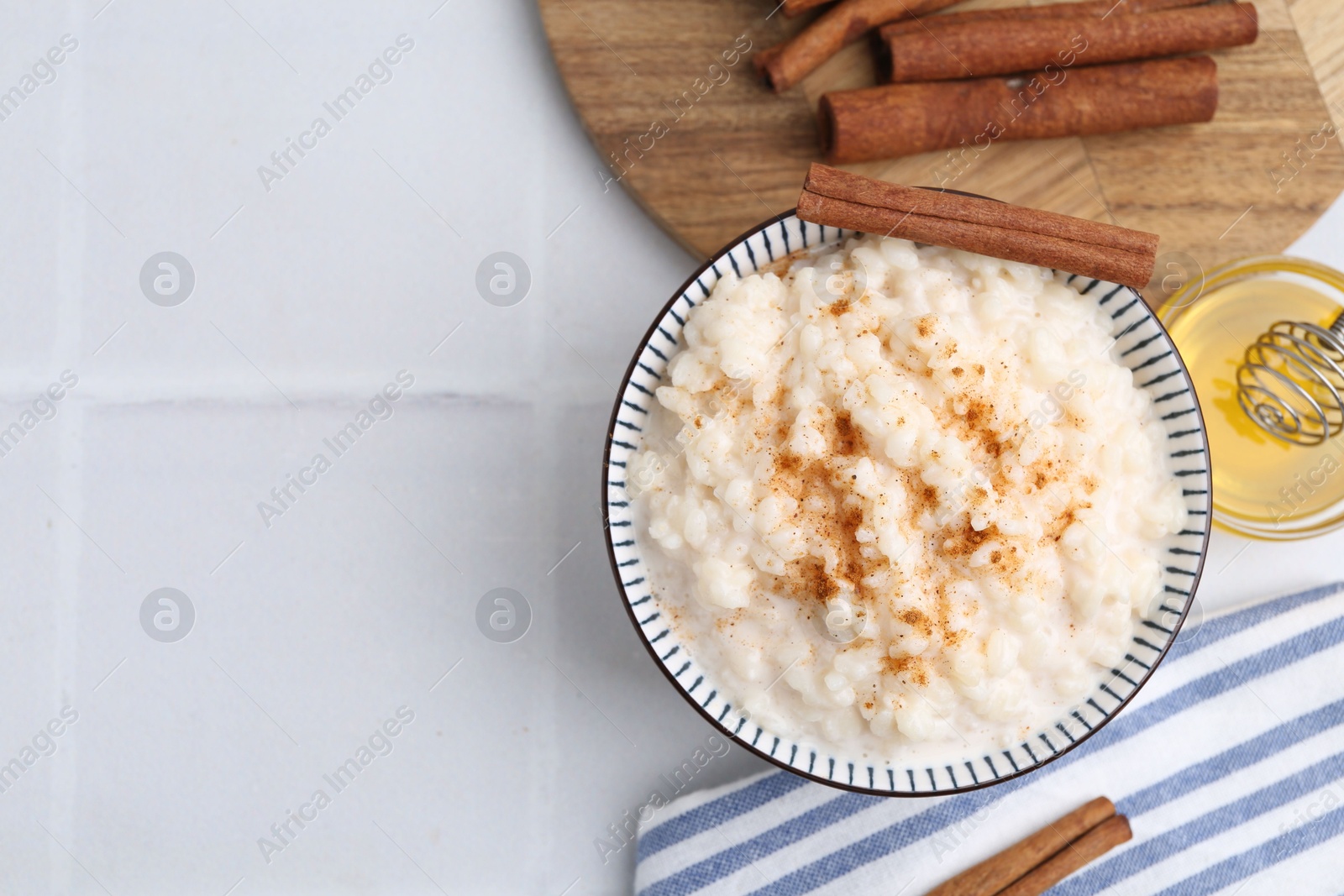 Photo of Tasty rice pudding with cinnamon served on white tiled table, flat lay. Space for text