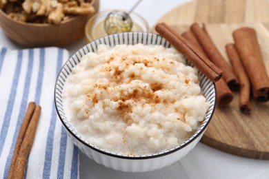 Photo of Tasty rice pudding with cinnamon served on white table, closeup