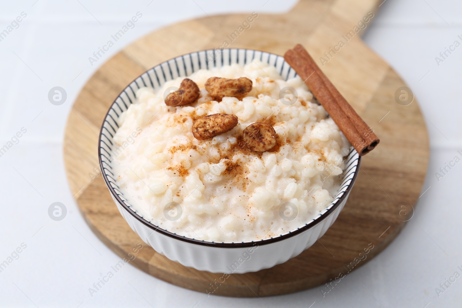 Photo of Delicious rice pudding with cinnamon and cashew nuts on white tiled table, closeup