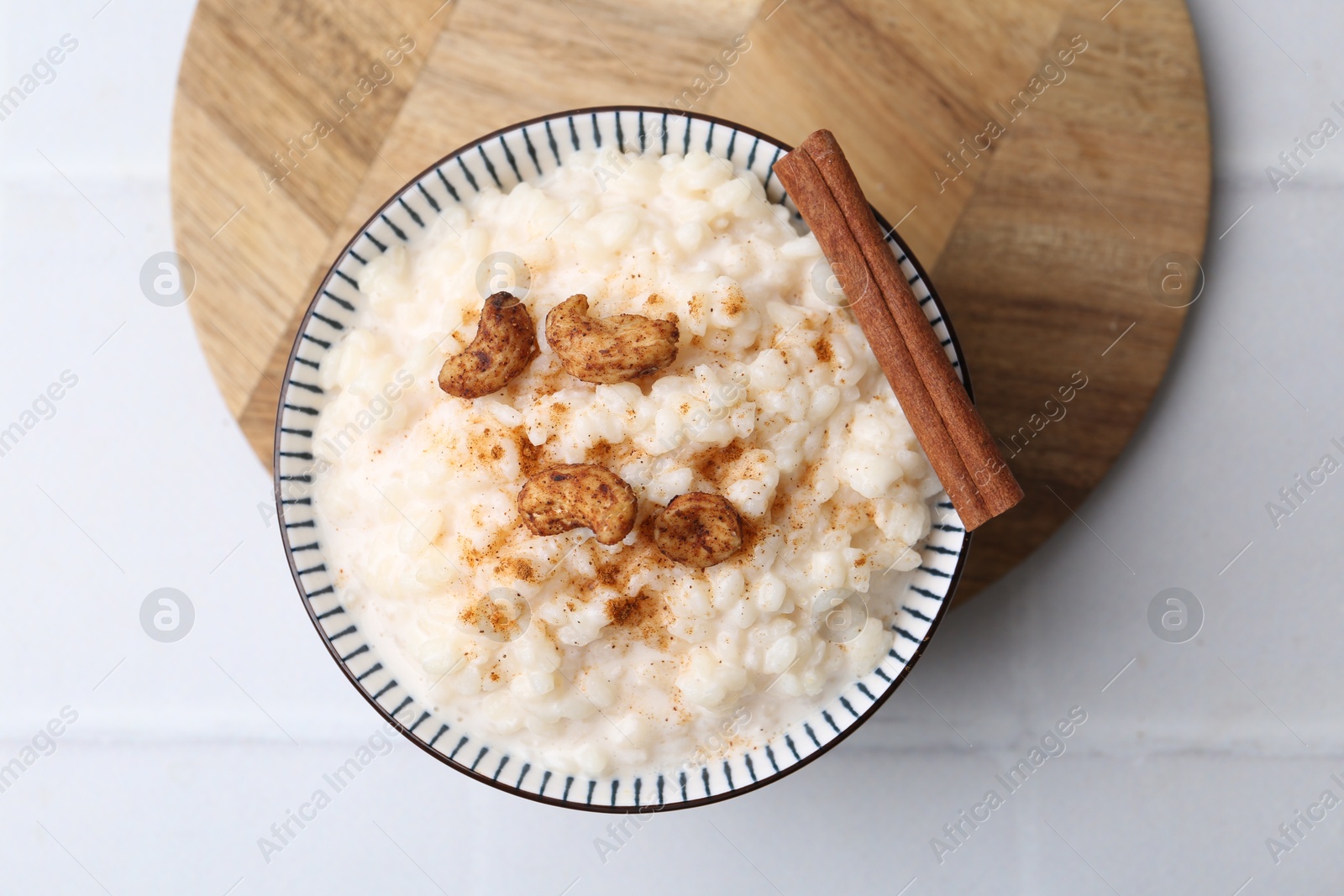 Photo of Delicious rice pudding with cinnamon and cashew nuts on white tiled table, top view