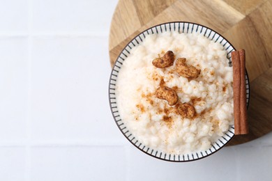 Photo of Delicious rice pudding with cinnamon and cashew nuts on white tiled table, top view. Space for text