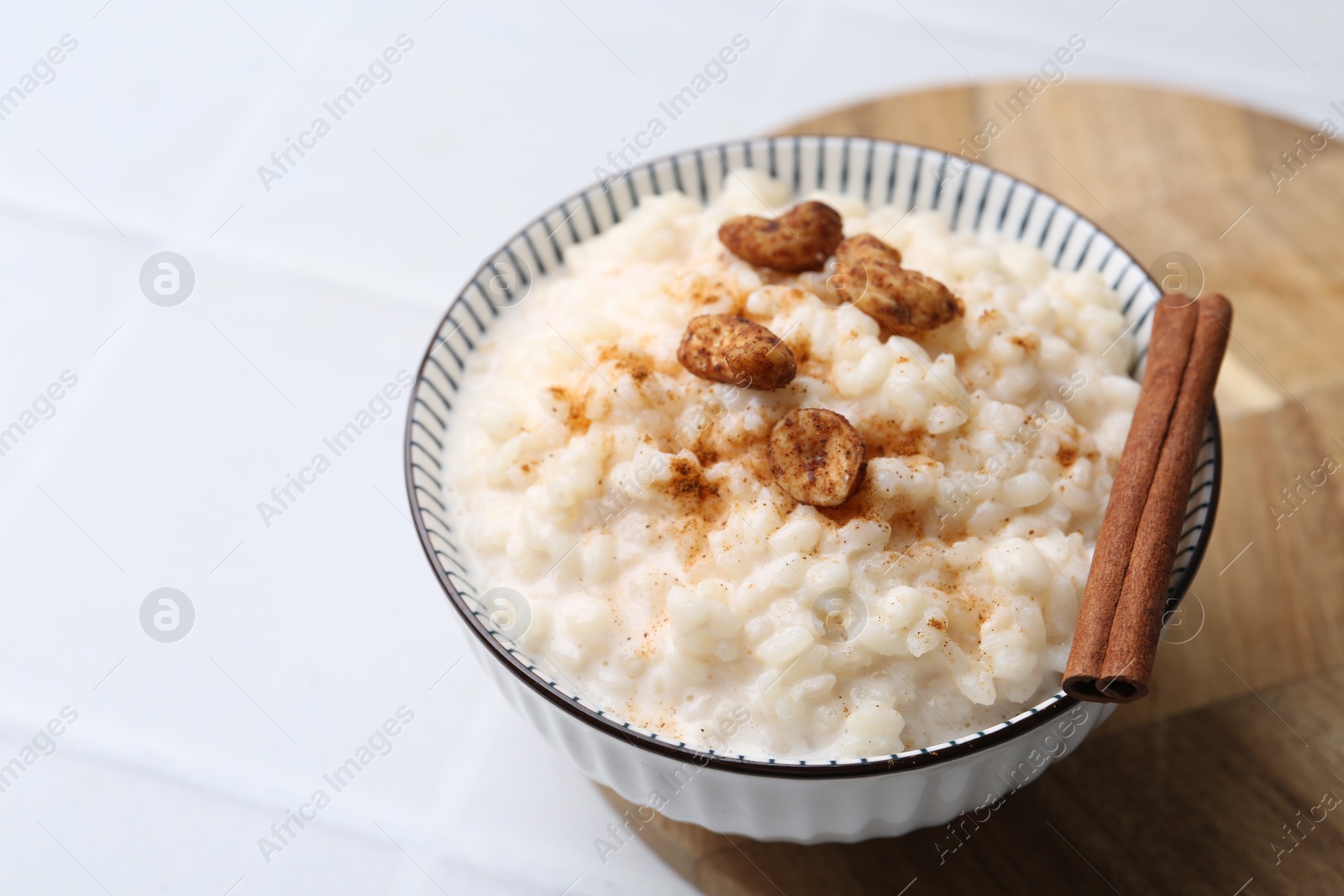 Photo of Delicious rice pudding with cinnamon and cashew nuts on white tiled table, closeup