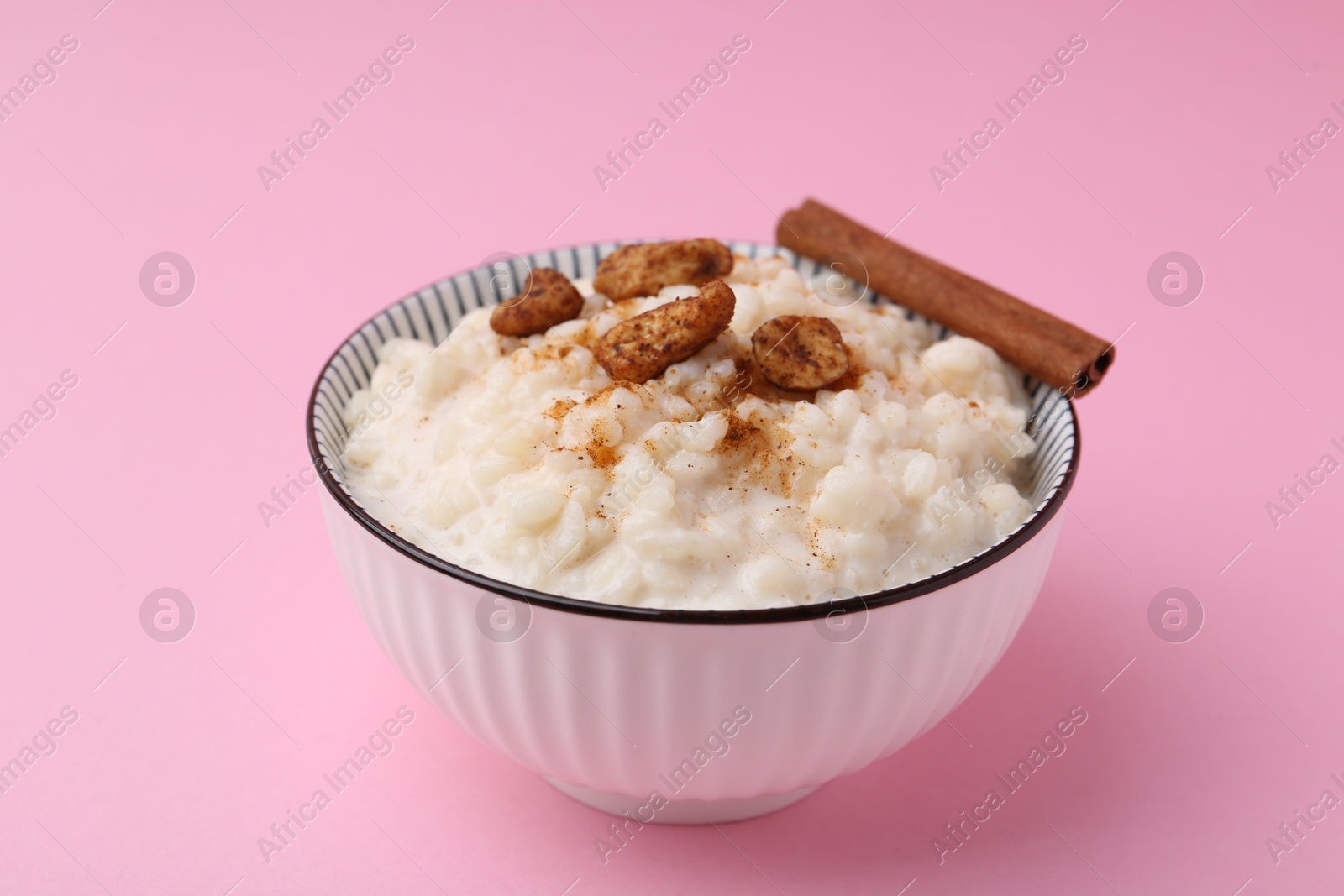 Photo of Delicious rice pudding with cinnamon and cashew nuts on pink background, closeup