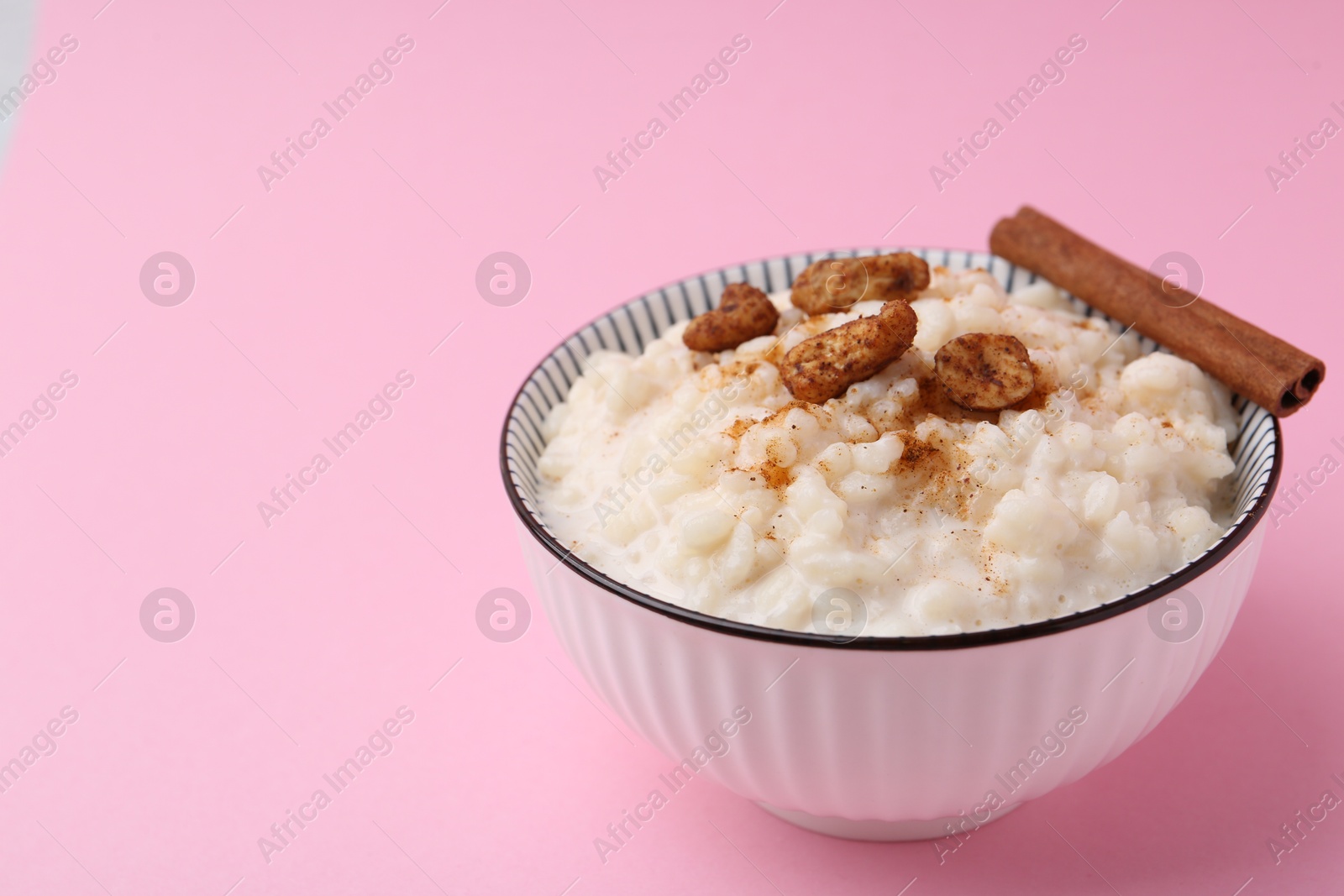 Photo of Delicious rice pudding with cinnamon and cashew nuts on pink background, closeup. Space for text