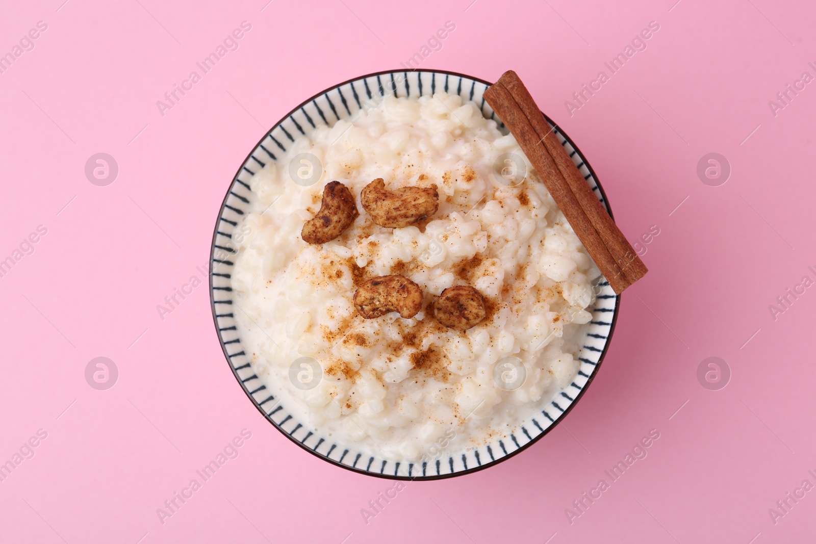 Photo of Delicious rice pudding with cinnamon and cashew nuts on pink background, top view