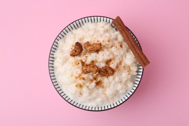 Photo of Delicious rice pudding with cinnamon and cashew nuts on pink background, top view