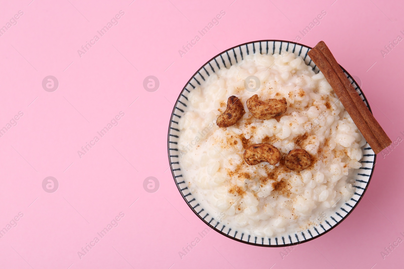 Photo of Delicious rice pudding with cinnamon and cashew nuts on pink background, top view. Space for text