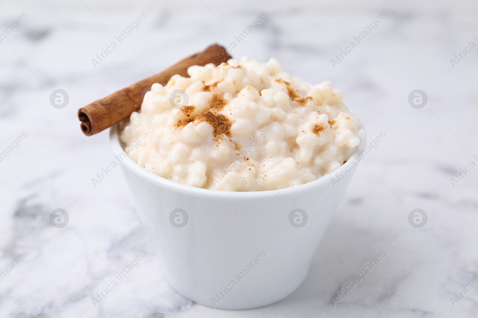 Photo of Tasty rice pudding with cinnamon on white marble table, closeup