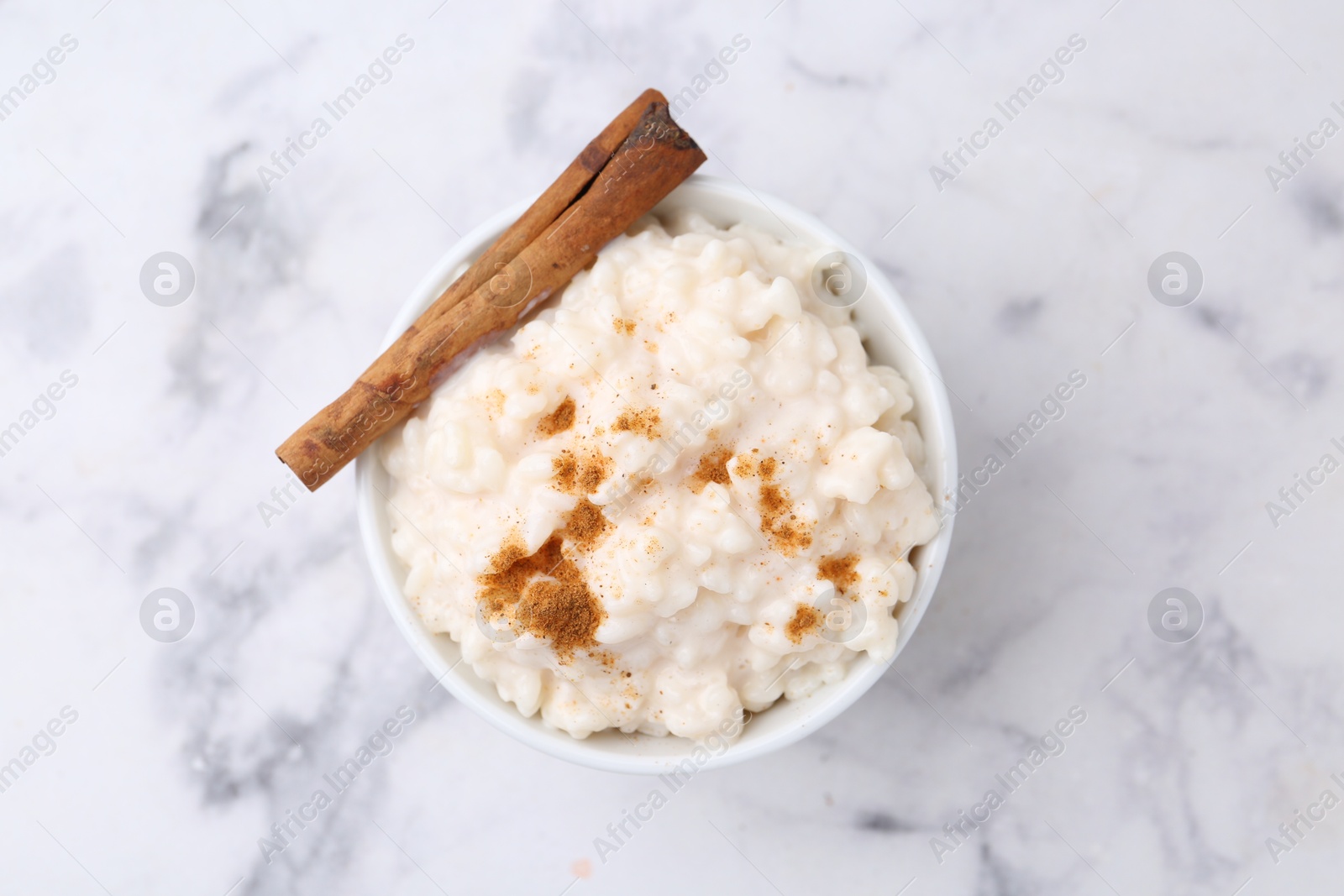 Photo of Tasty rice pudding with cinnamon on white marble table, top view