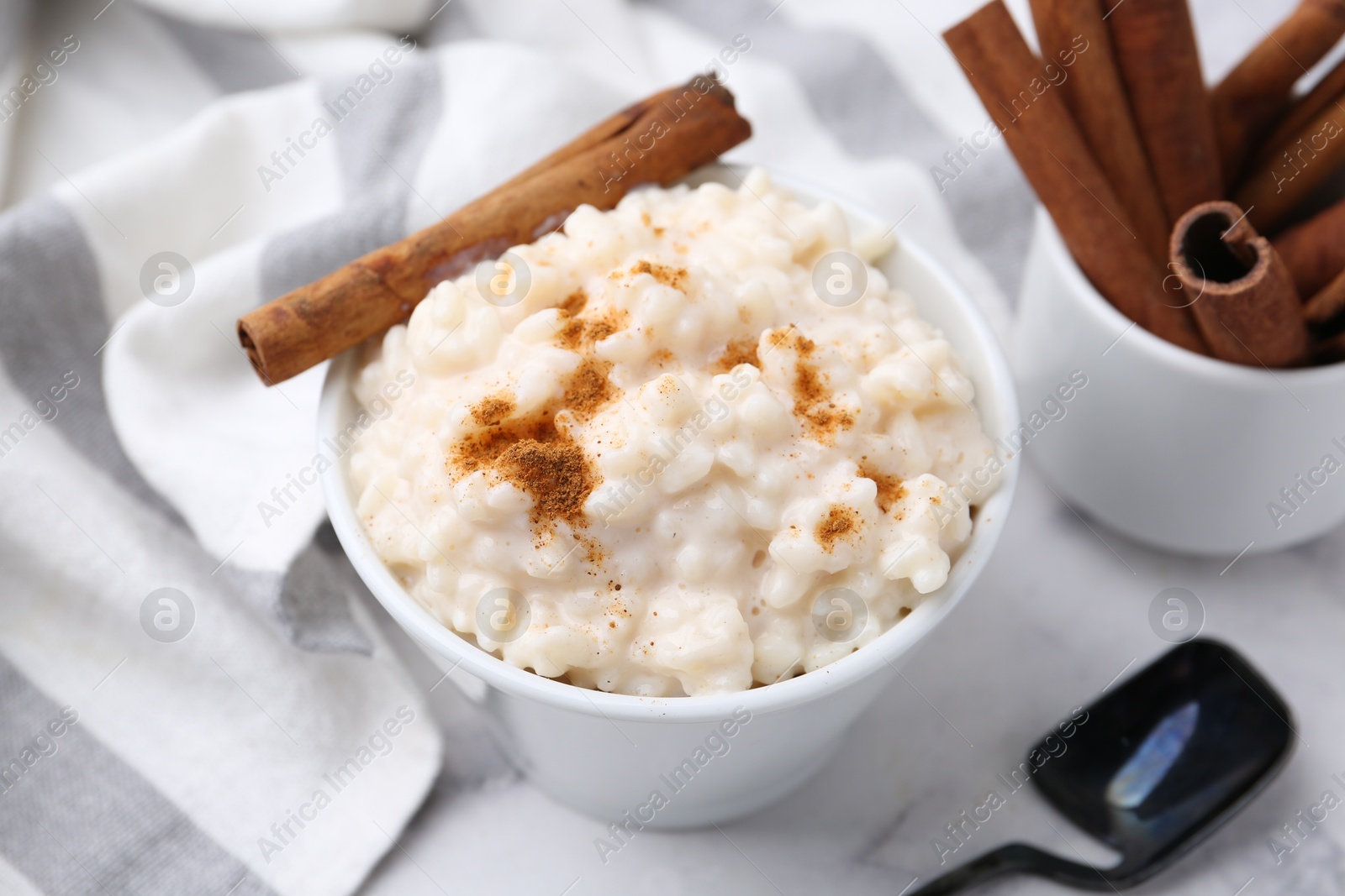 Photo of Tasty rice pudding with cinnamon served on white marble table, closeup