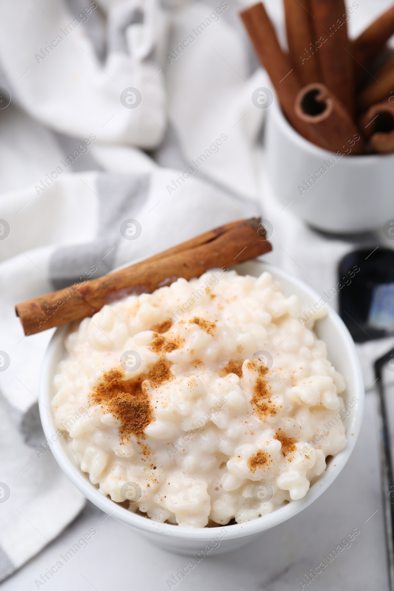 Photo of Tasty rice pudding with cinnamon served on white table, closeup