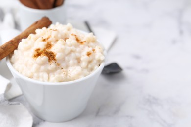 Photo of Tasty rice pudding with cinnamon served on white marble table, closeup. Space for text