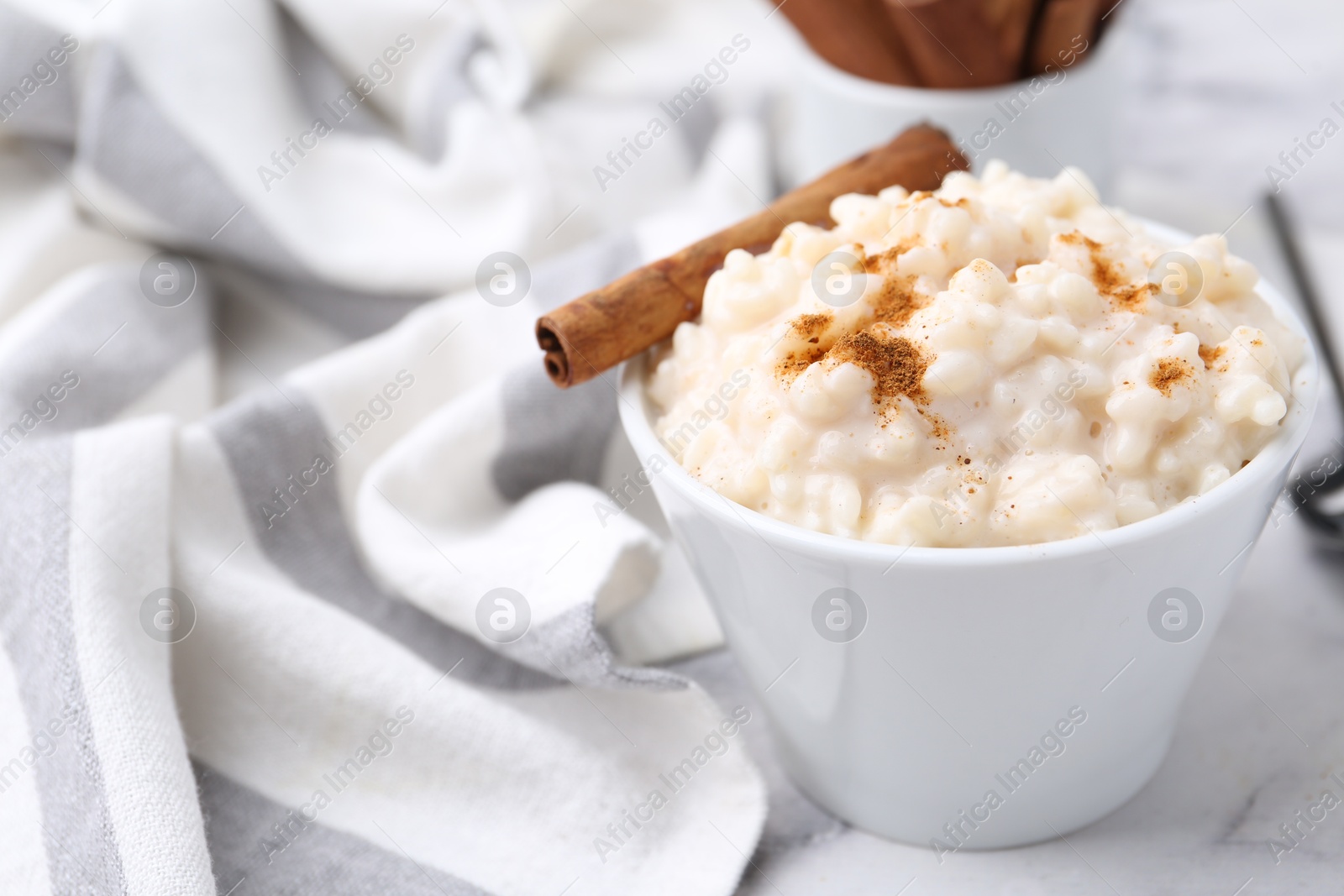 Photo of Tasty rice pudding with cinnamon served on white table, closeup. Space for text