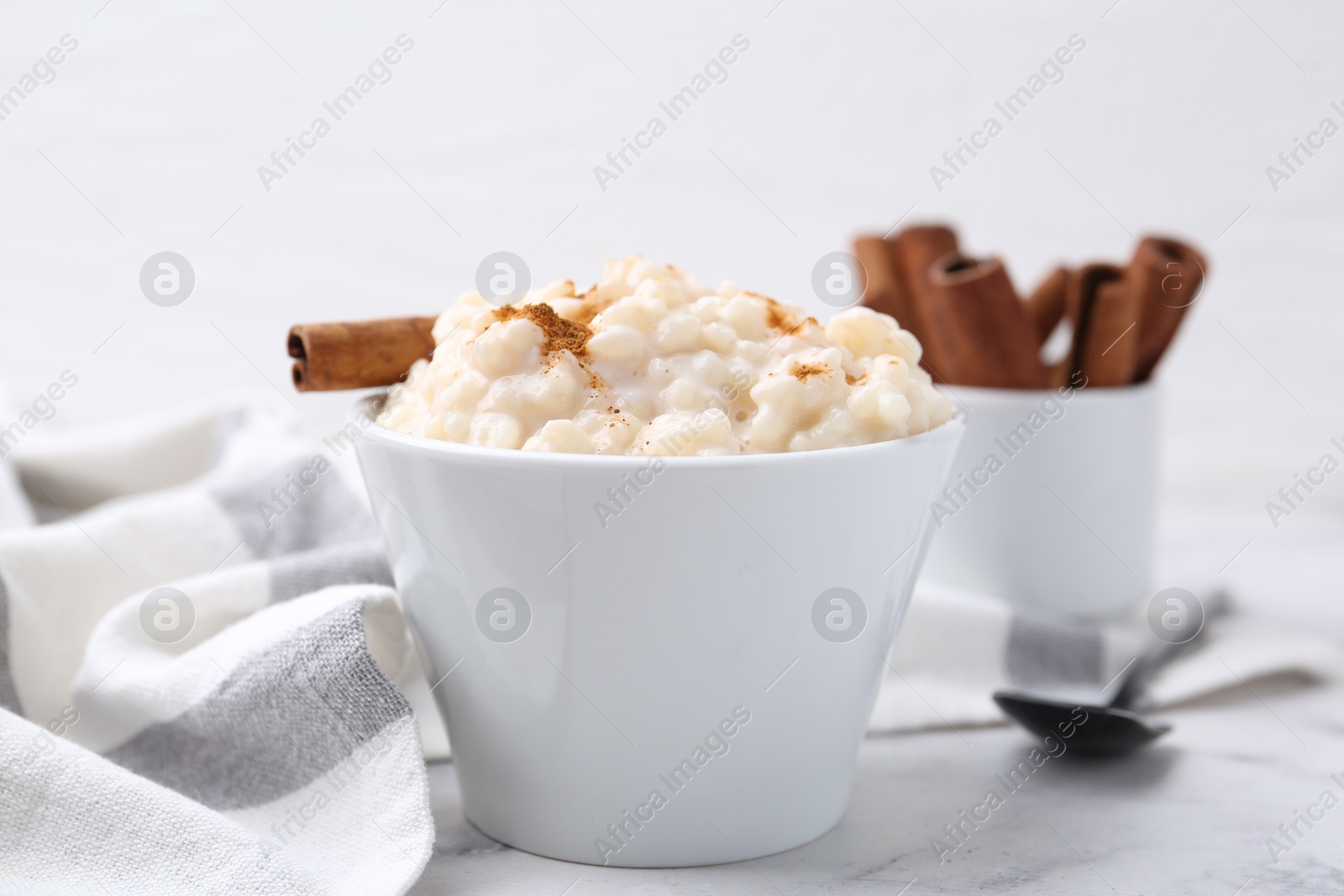 Photo of Tasty rice pudding with cinnamon served on white table, closeup