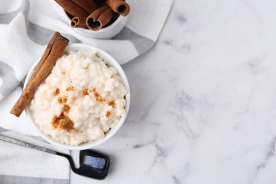 Photo of Tasty rice pudding with cinnamon served on white marble table, flat lay. Space for text