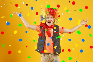 Image of Happy boy dressed like clown under falling confetti on orange background. Party time