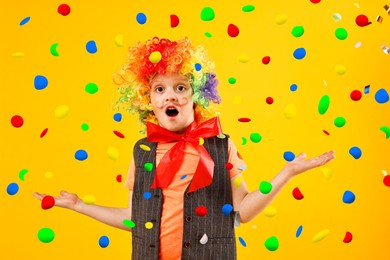 Image of Cute boy dressed like clown under falling confetti on orange background. Party time