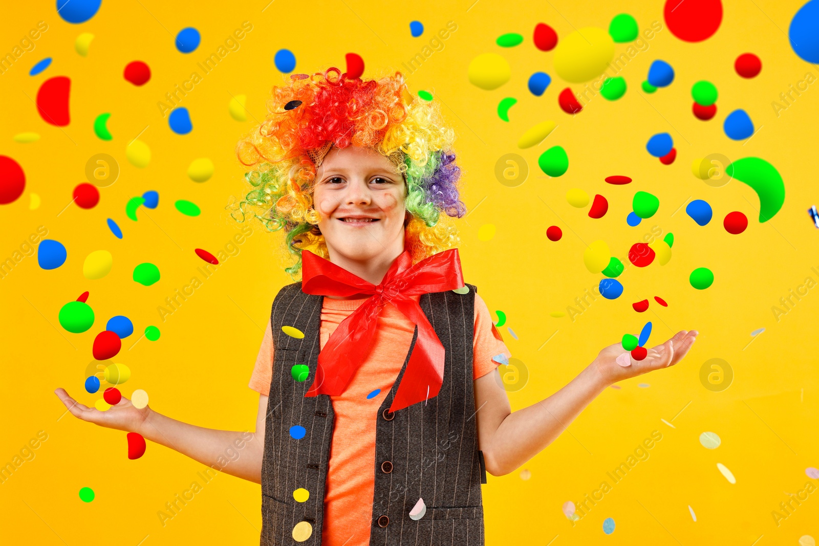 Image of Happy boy dressed like clown and confetti on orange background. Party time