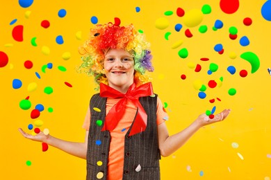 Image of Happy boy dressed like clown and confetti on orange background. Party time