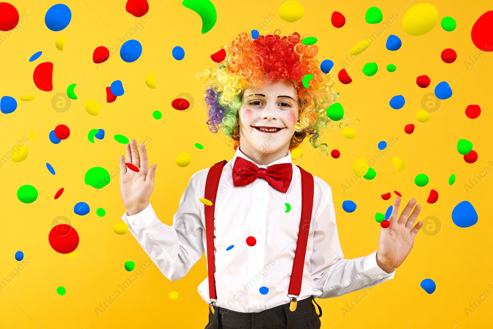 Image of Happy boy dressed like clown under falling confetti on orange background. Party time