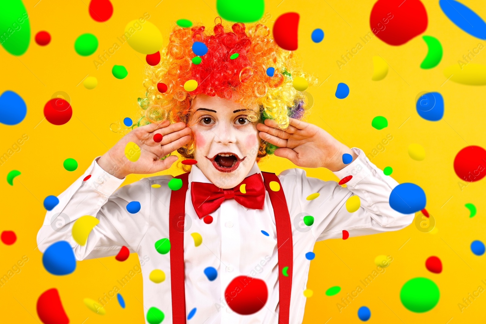 Image of Cute boy dressed like clown under falling confetti on orange background. Party time