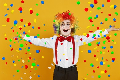 Image of Happy boy dressed like clown under falling confetti on orange background. Party time