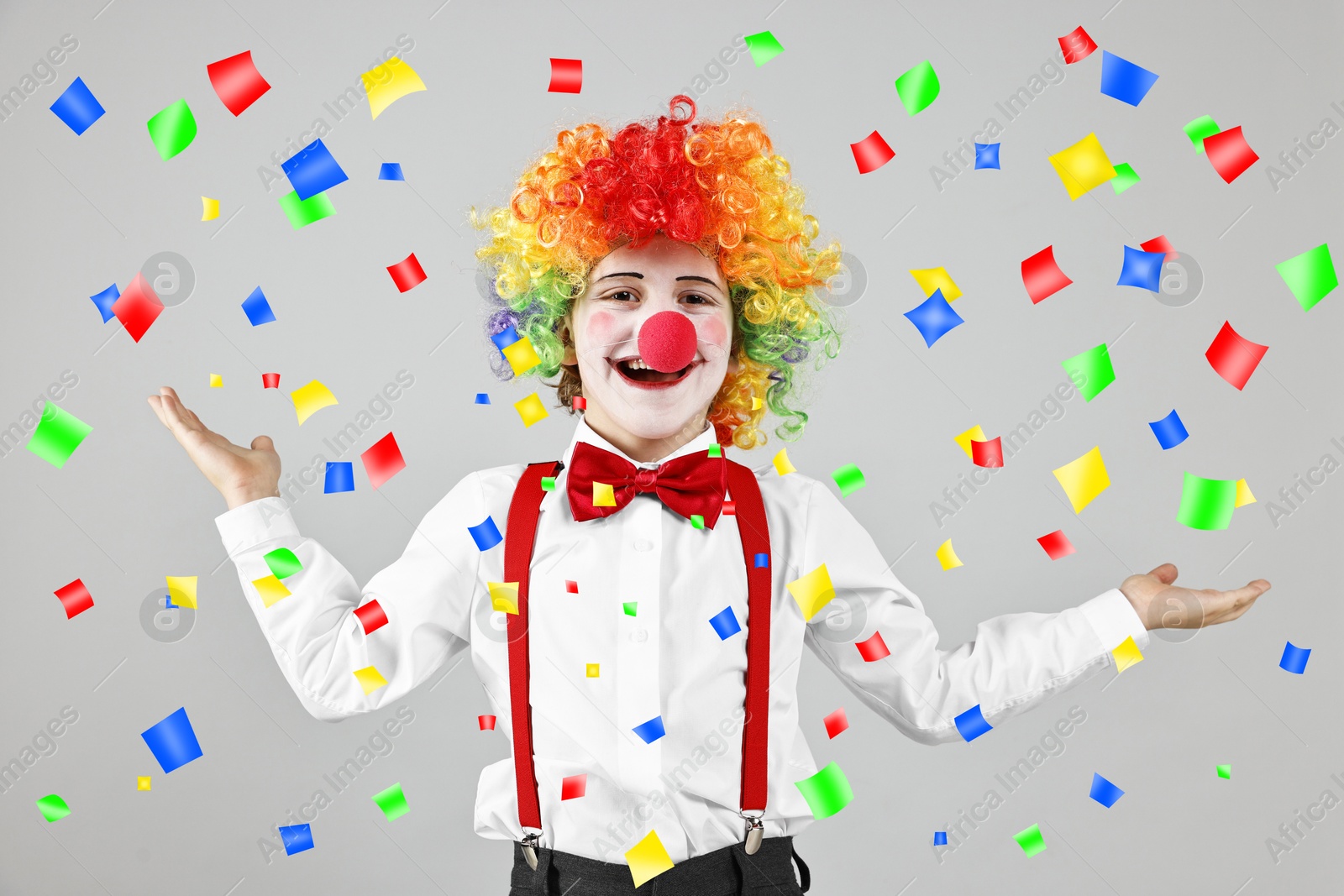 Image of Happy boy dressed like clown under falling confetti on grey background. Party time