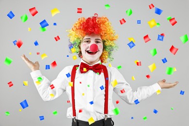 Happy boy dressed like clown under falling confetti on grey background. Party time