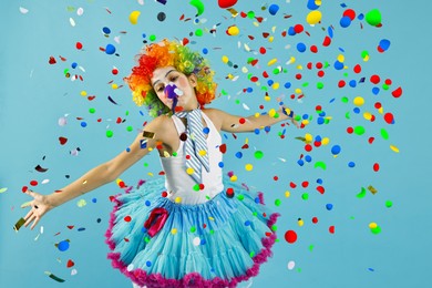 Image of Happy girl dressed like clown under falling confetti on light blue background. Party time