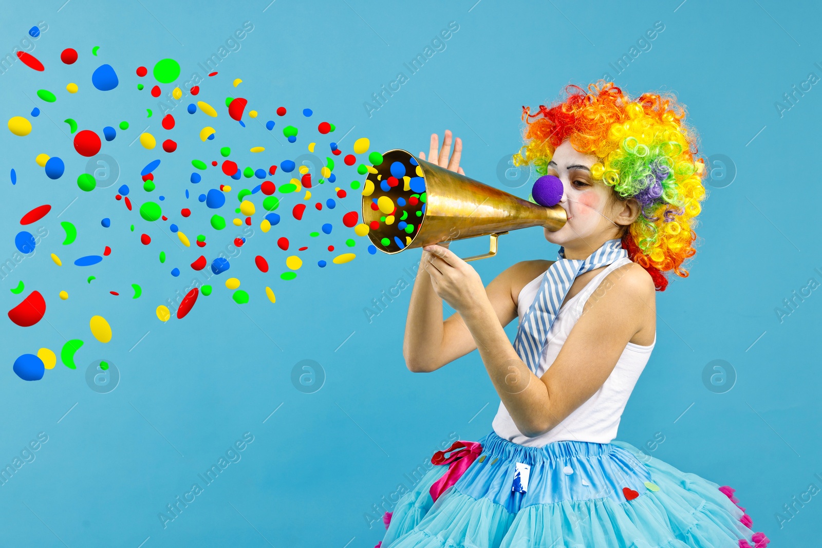 Image of Cute girl dressed like clown shouting in megaphone with confetti flying out of it on light blue background. Party time